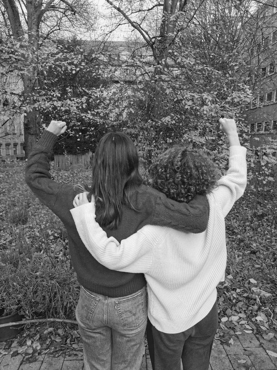 Two women standing side by side, one having her fist in the air